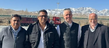 Businessmen posing outdoors with a logistics truck and snow-capped mountains in the background.