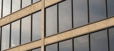 Detail of modern architectural glass facade reflecting overcast sky, clean lines, minimalist editorial photography, warm sand tones