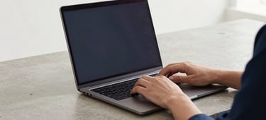 Hands typing on a sleek laptop on a clean concrete desk, soft natural overcast daylight, professional minimalist setup