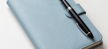 A minimalist, high-angle shot of a clean, organized desk featuring a sleek leather notebook and a high-end fountain pen. The aesthetic is professional and academic, set in a bright North American study with a color palette of soft off-white and light blue.