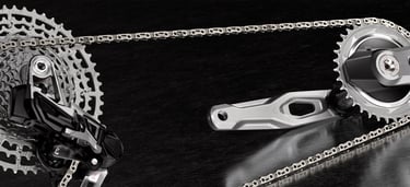 Close-up of a silver bicycle drivetrain featuring a high-performance cassette, chain, and crankset on a dark surface.