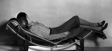 Black and white photo of a person reclining on a modern chaise longue, reflecting Charlotte Perriand