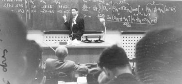 Vintage black and white photo of a professor teaching physics equations on a chalkboard.