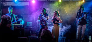 Live band performing a concert on a foggy stage with colorful spotlighting and vocalists.