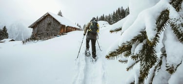 persona caminando en al nieve con cabaña de fondo