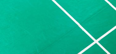 Top down view of a green badminton court surface with white boundary line markings.