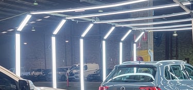 Modern LED arch lighting system illuminating cars in a professional automotive detailing and inspection garage.