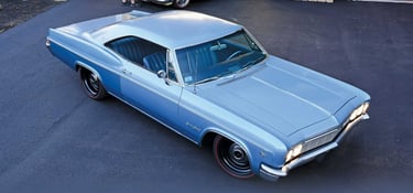 A classic 1966 light blue Chevrolet Impala SS hardtop parked on asphalt with redline tires.