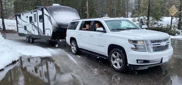 rv rental in the snow being towed behind a SUV with a big happy family in the windows