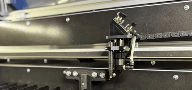 Zdjęcie wnętrza lasera CO2, przedstawia stół nożowy oraz głowicę 