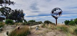 Verdigris metal globe sculpture on the beach with a mother whale and her calf in the middle of it