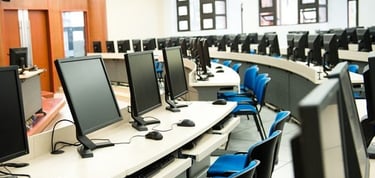 Modern university computer lab featuring rows of monitors and blue chairs for student learning.