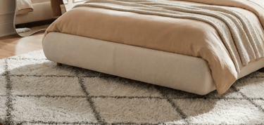 Cream upholstered platform bed frame on a plush trellis area rug in a modern bedroom.