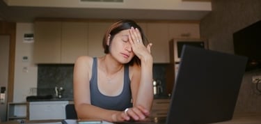 Stressed woman rubbing her eyes while working on a laptop at home to relieve digital eye strain.