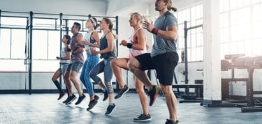A diverse group of people doing high knee cardio exercises during a group fitness class in a gym.