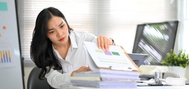 A focused businesswoman reviews financial data charts and paperwork at an office desk.