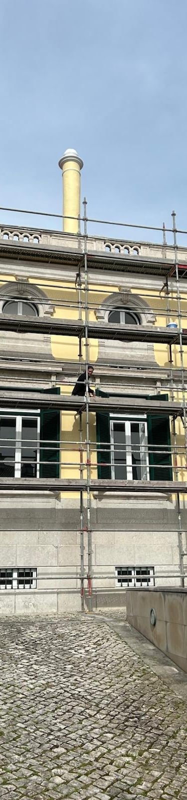Exterior of a historic yellow building with metal scaffolding for facade restoration and maintenance.