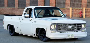 Custom white classic Chevrolet C10 pickup truck with lowered suspension and black wheels parked by a brick building.