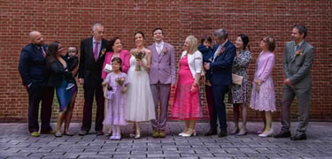 Smiling wedding party and family members posing for a group portrait against a red brick wall.