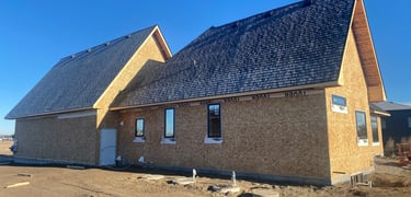 New house construction with plywood sheathing, dark shingle roof, and installed windows under a clear blue sky.