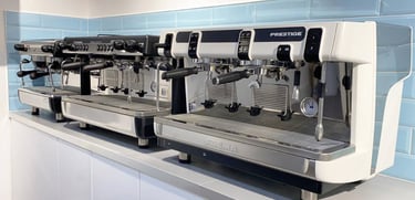 A dual espresso machine setup with multiple coffee brewing handles and steam wands, mounted on a counter with a light blue ti