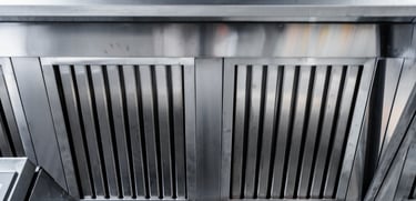 A stainless steel commercial kitchen exhaust hood with vertical slats designed for ventilation.