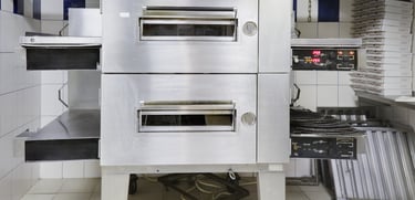 A stainless steel double-deck pizza oven with trays extended and control panels showing temperature settings.