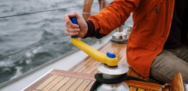 a man in a red jacket is holding a winch on a sailing boat