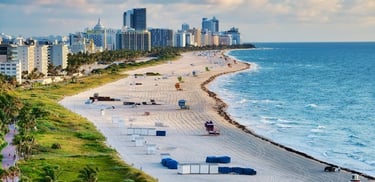 Vista aérea de uma longa praia com prédios ao fundo e mar azul em Miami