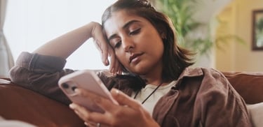 A bored woman lounging on a couch while scrolling through her smartphone at home.