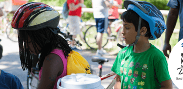 Two kids standing together wearing helmets