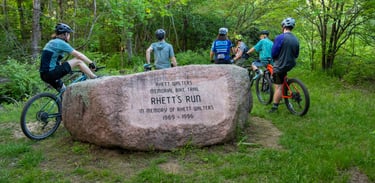 People stopped on their bikes next to a large rock engraved with the memorial info of "Rhett's Run"