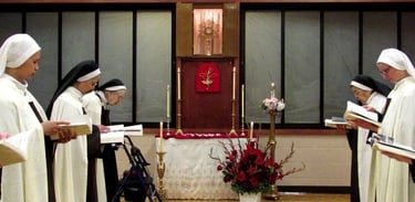 Carmelite nuns praying in the choir with the Blessed Sacrament exposed in the background.