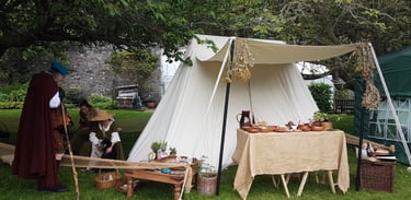 reenactors talking beside a medieval tent with a table of herbal remedies