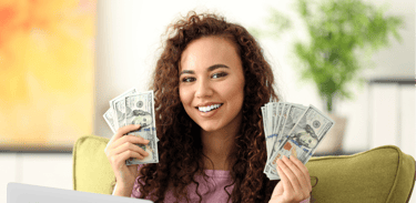 a woman sitting on a couch holding a laptop and holding money