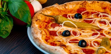 Steinofen-Peperoni-Pizza mit schwarzen Oliven, Zwiebeln und scharfen grünen Paprika auf einem rustik