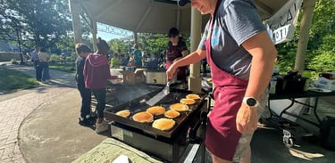 Kids in the background of a person flipping pancakes on a griddle in a park