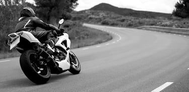 Rear right view of a motorcycle as it take a left hand bend with a road position that gives the view