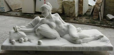 Hand-carved white marble sculpture of a reclining nude woman resting on pillows with stone apples.