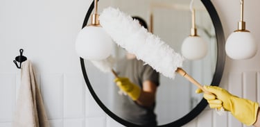 Personne nettoyant un luminaire avec un plumeau devant un miroir