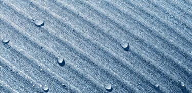 Macro shot of the crisp ice-blue evaporative weave texture, water droplets bead-blasting off the fabric under bright high-contrast sunlight, sharp 35mm detail