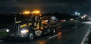 Caminhão-guincho moderno de plataforma, com luzes de emergência acesas, em rodovia noturna. Foco no caminhão, com o horizonte baixo e espaço negativo à esquerda. Estilo: fotografia automotiva dramática, alto contraste, tons preto e amarelo, foco nítido.