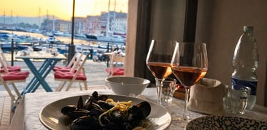 Seafood pasta with mussels and glasses of rose wine served at a waterfront restaurant at sunset.