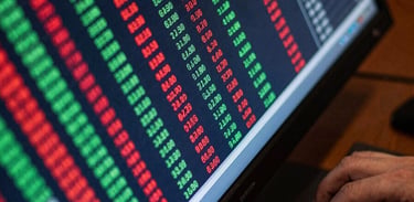 Close-up overhead of a trading terminal screen, electric green and red ticker rows mid-scroll, hands resting on keyboard edge, cool blue-white screen glow, dark desk surface visible at corners, tight frame on the live data