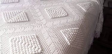 Colcha blanca vintage de ganchillo con patrones geométricos de punto texturizado sobre una cama.