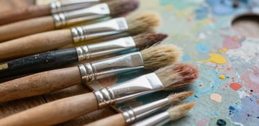An array of paint brushes and colorful palettes on a wooden table, soft focus, inspiring and artistic atmosphere conveying creativity.
