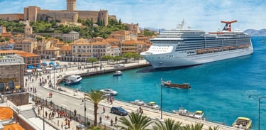 Navio de cruzeiro atracado em Heraklion, com movimentação de passageiros e portos de serviços ao fundo.