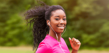 Une jeune femme noire aux cheveux naturels et un haut de sport rose qui fait son jogging