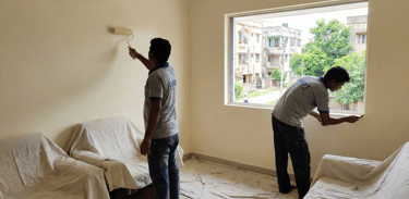 Professional house painters applying off-white paint to interior walls with a roller and brush.
