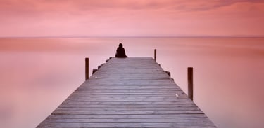 A person sitting alone at the end of a jetty on a calm evening. The scene depicts the Lonely Art of Art